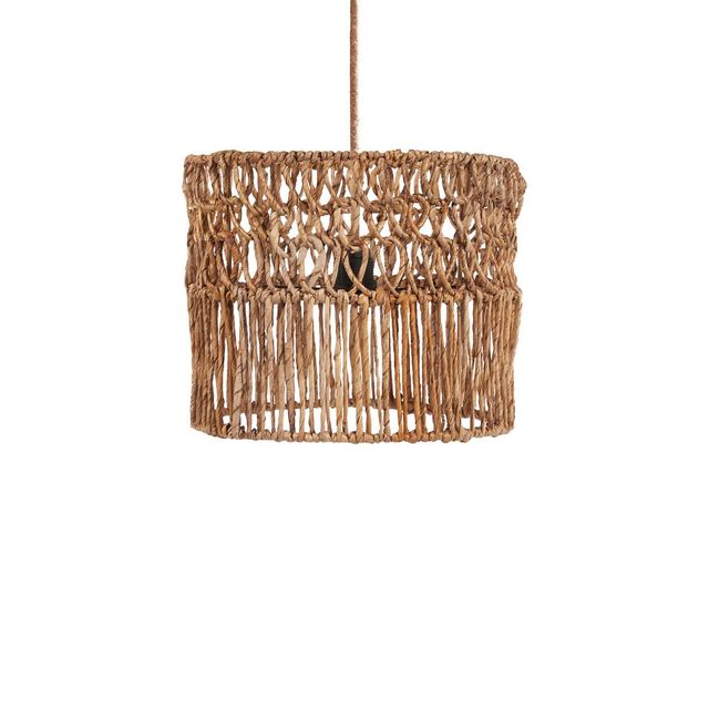 A cylindrical woven rattan pendant light with a warm glowing bulb, hanging in a rustic, warm-toned Mediterranean-style kitchen with beige plaster walls, wooden cabinets, and a stone countertop.