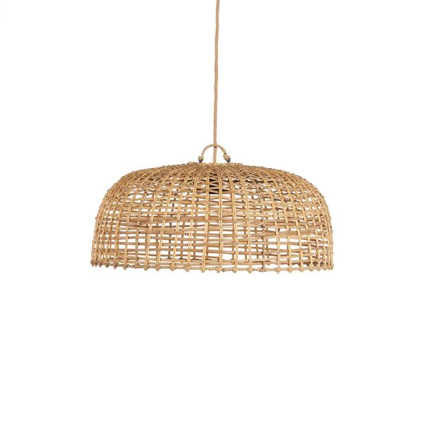 A woven rattan dome pendant light hangs over a rustic wooden dining table in a warm, sunlit room with cream walls, wicker chairs, and potted plants.