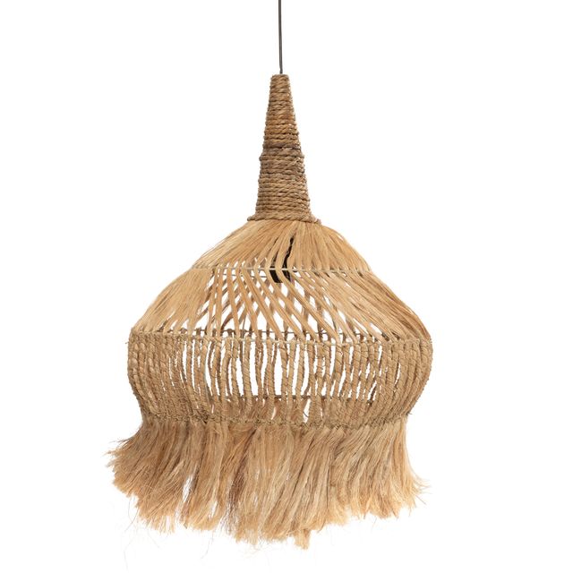 A woven natural-fiber pendant light with fringe hangs over a rustic wooden table on an outdoor patio overlooking the sea.